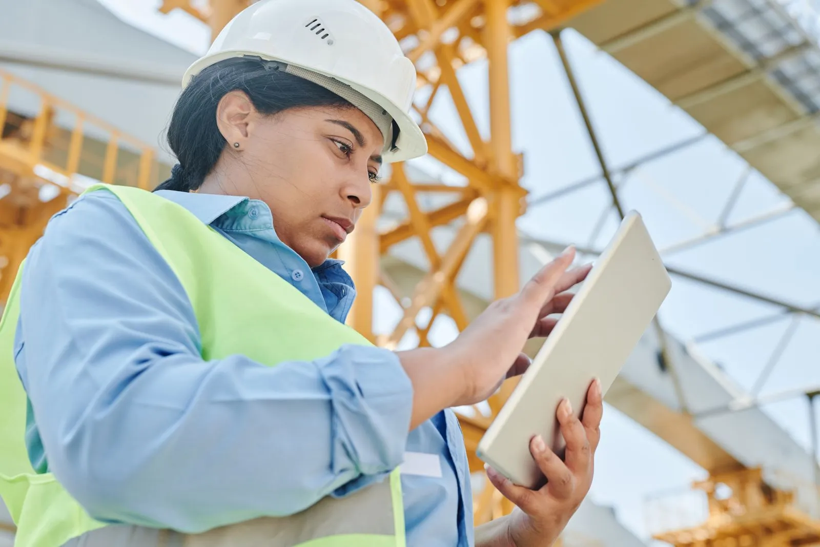 A woman in a hard hat and safety vest checks notes on a tablet at a job site